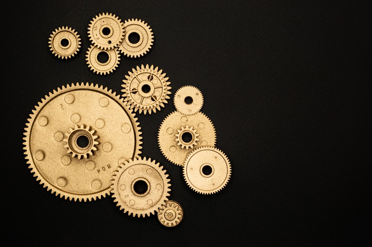 ours-journey Close-up of gold gears arranged on a black backdrop, symbolizing teamwork and technology.