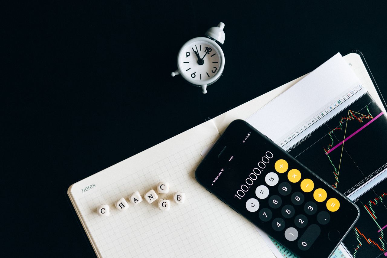 The Art of Drawing Readers In: Your attractive post title goes here Notebook with an iPhone displaying 100,000,000, desk clock and financial charts suggesting market analysis.